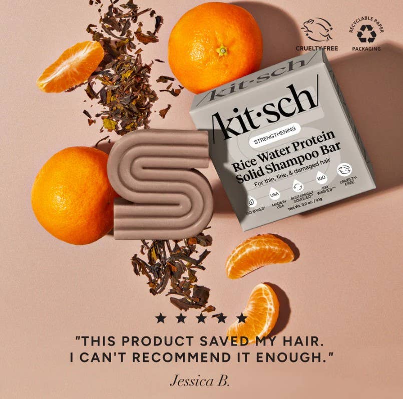 A KITSCH Rice Water Protein Solid Shampoo Bar for Hair Growth (3.2oz) is pictured with tea leaves and tangerines on a beige background, alongside a customer testimonial praising how the bar saved their hair, increased volume, and comes highly recommended. Featuring cruelty-free and recyclable packaging icons, it's an eco-friendly addition to your haircare routine.