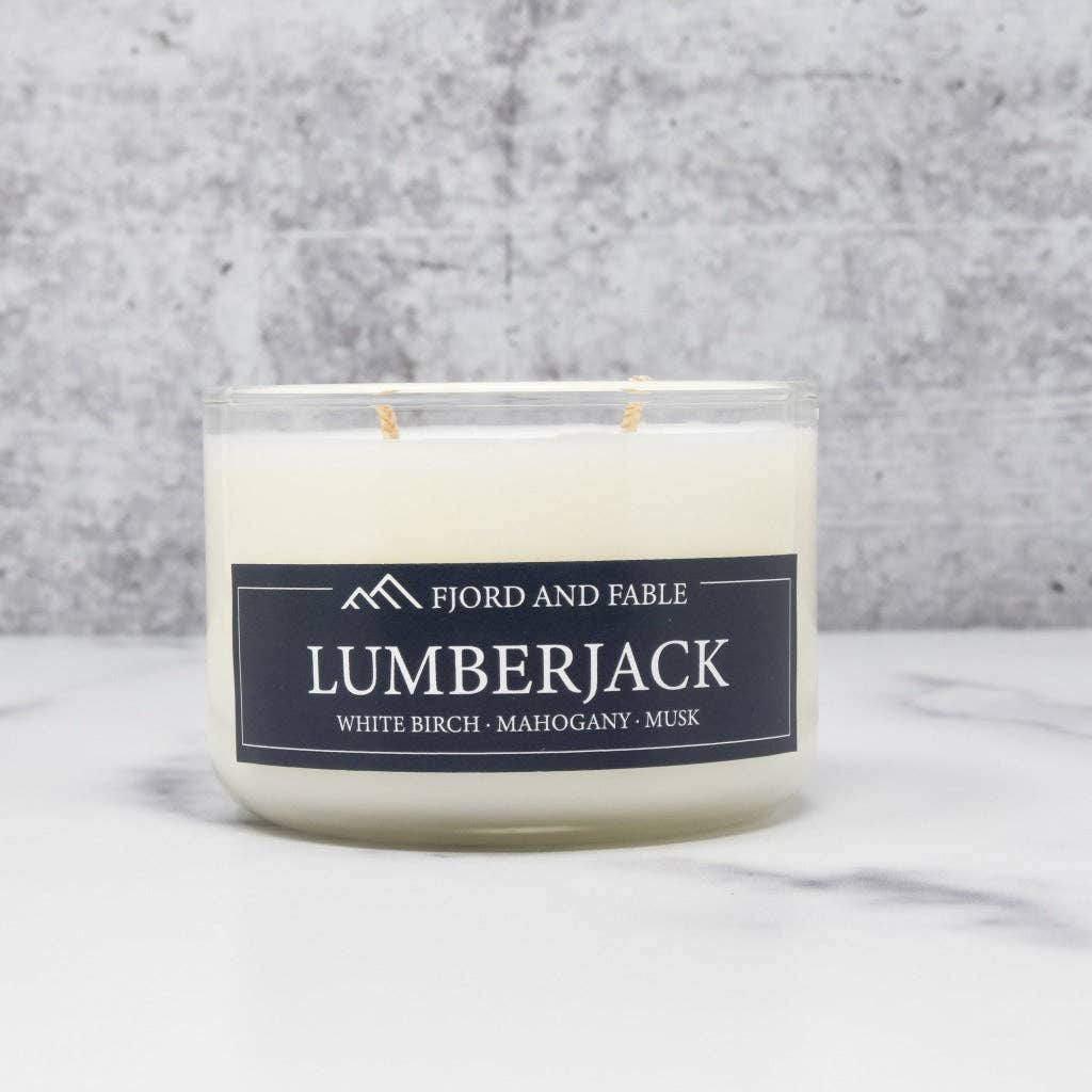 A 4oz white soy wax Lumberjack candle by Fjord and Fable, featuring white birch, pine, bergamot, and moss scents in a clear jar, set against a gray background.