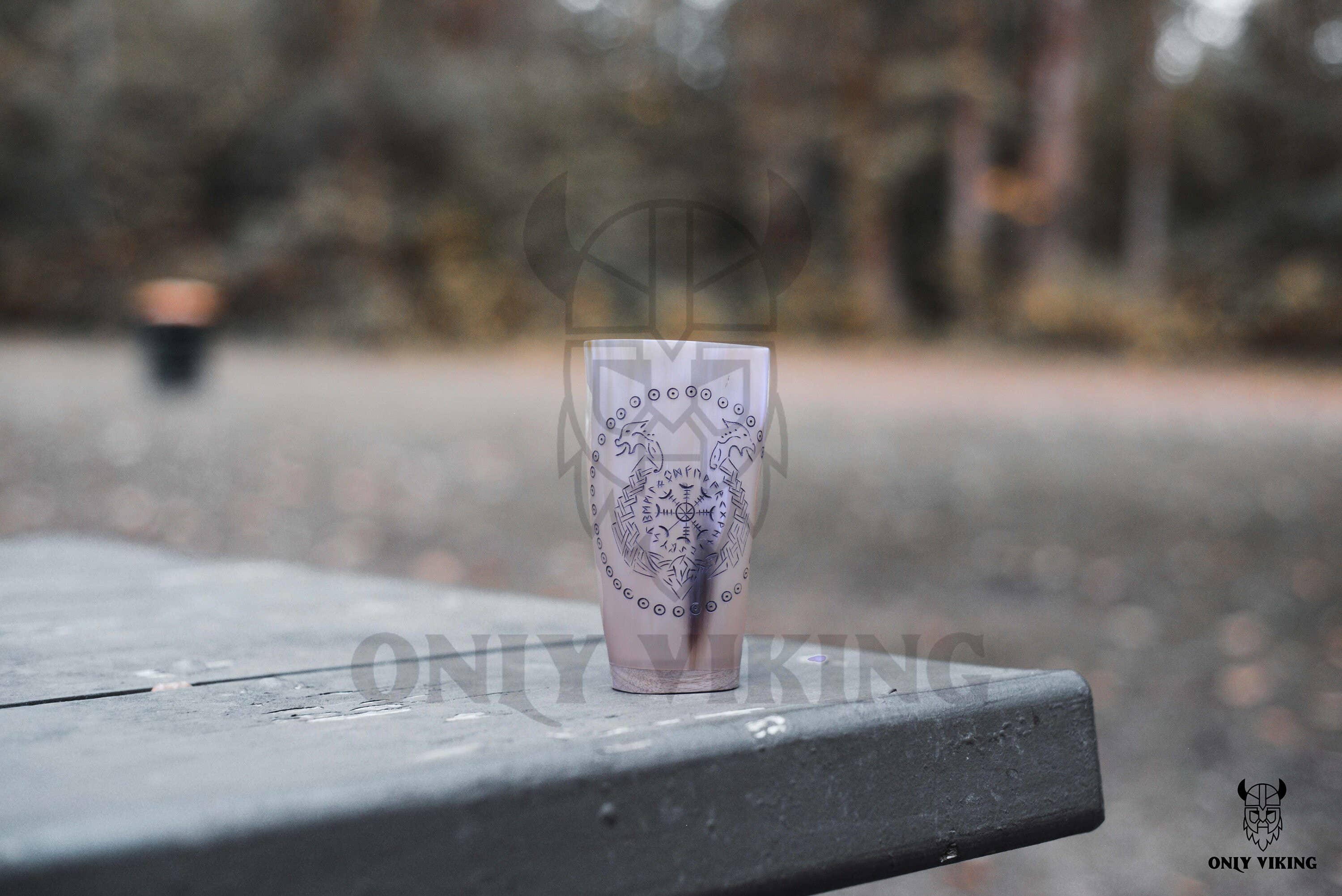 The Horn Mug: Beer Stein Drinking Horn Mug Tree of Life 6-9 oz, inspired by a Viking ox horn, sits on an outdoor picnic table; blurred trees and a trash bin appear in the background.