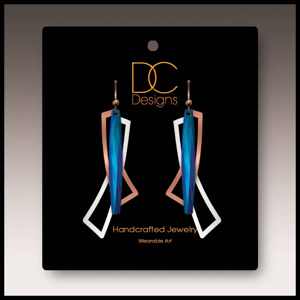 A pair of modern blue, silver, and copper geometric open wings earrings (1.75"), handmade in stainless steel, displayed on a black card labeled “DC Designs Handcrafted Jewelry Wearable Art.”.