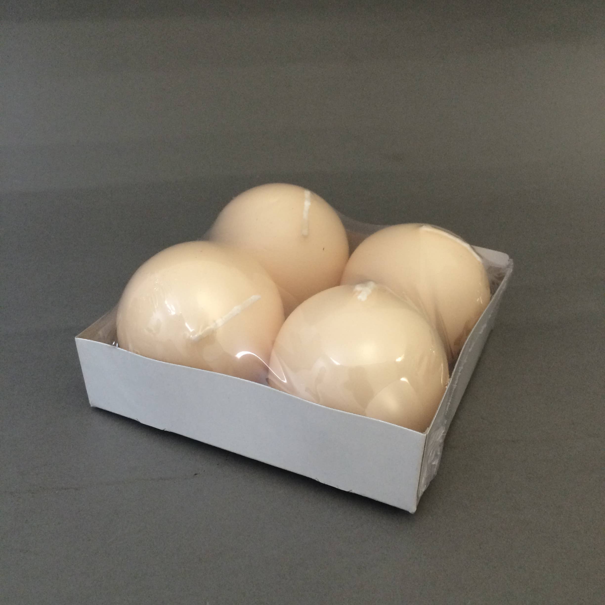 A pack of four unscented, round ivory Champagne Ball Candles (2.5" diameter) sits in a white cardboard tray wrapped in clear plastic—perfect for elegant decorative displays.