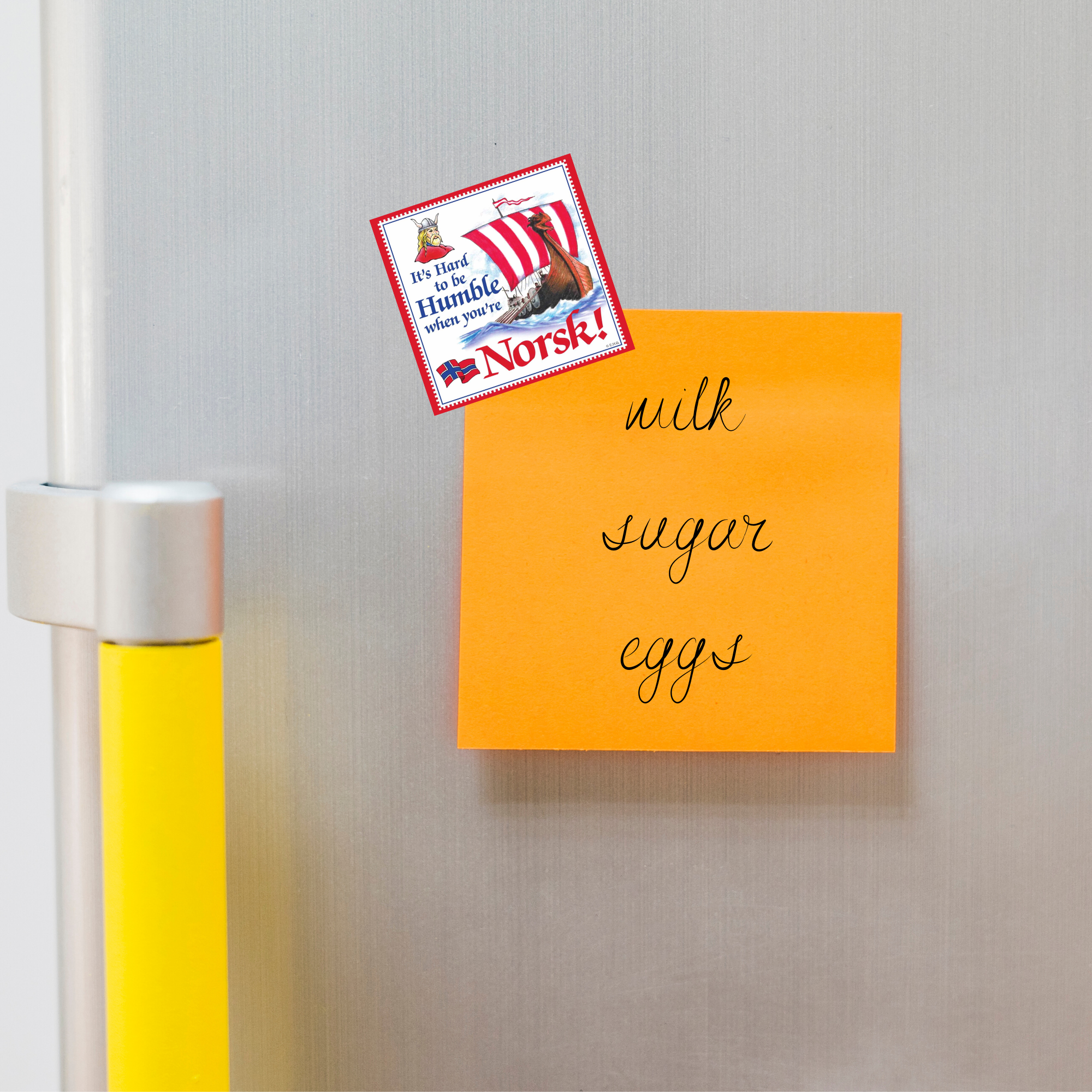 A yellow sticky note listing milk, sugar, and eggs is attached to a silver fridge next to the It’s Hard to be Humble When You’re Norsk! Norwegian refrigerator magnet (3 square).