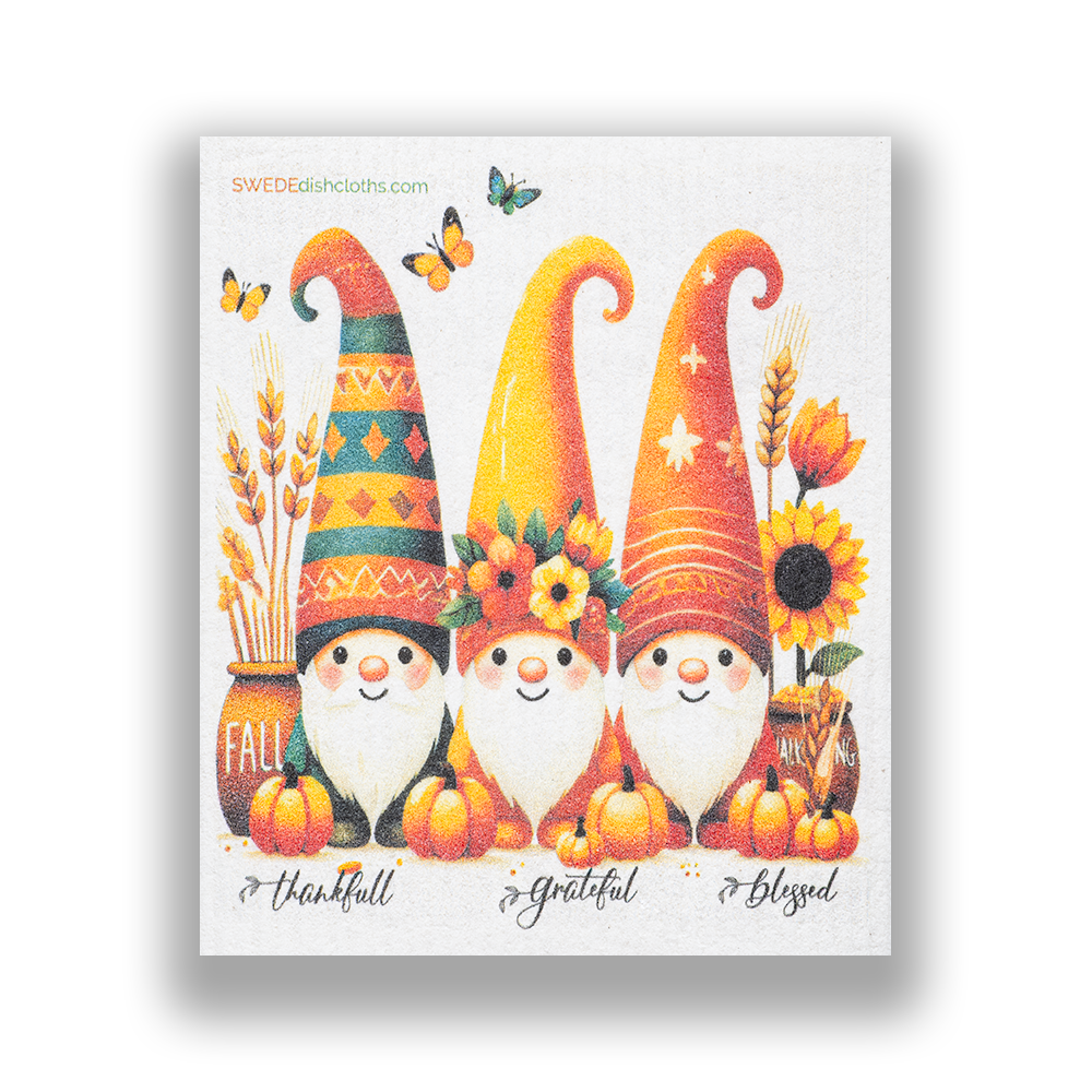 Reusable dish towel featuring three autumn gnomes surrounded by pumpkins, sunflowers, and butterflies against a background of vivid fall colors.