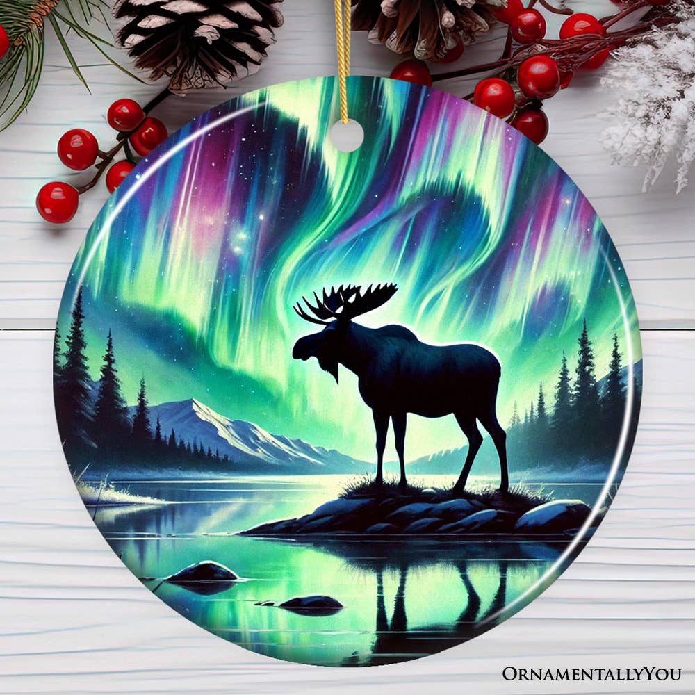 The Ornament: Majestic Moose Under Northern Lights Christmas Tree Ornament depicts a moose by a lakeside, illuminated by vibrant northern lights and surrounded by snow-dusted pinecones and red berries, ideal for nature-themed holiday decor.