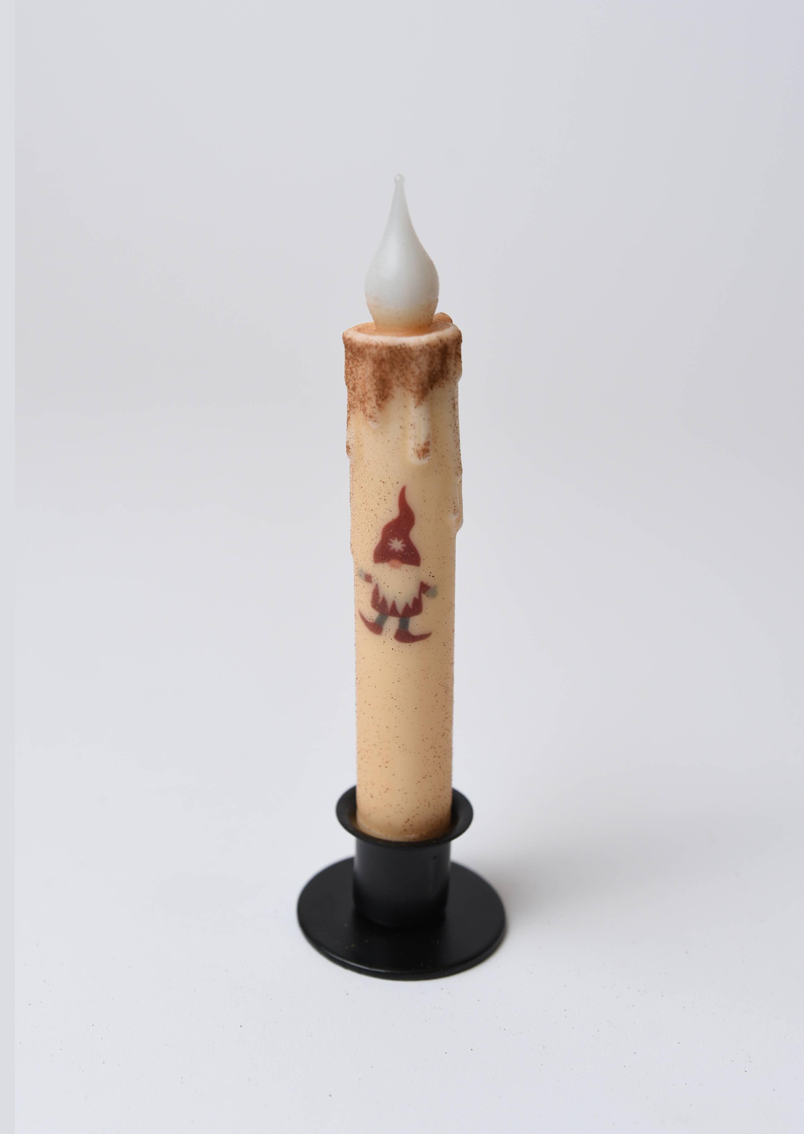 The Christmas Gnome LED Timer Taper Candle: Cinnamon Dusted has a faux flame in a black holder, runs on batteries, features a timer, and displays a gnome in a red hat.