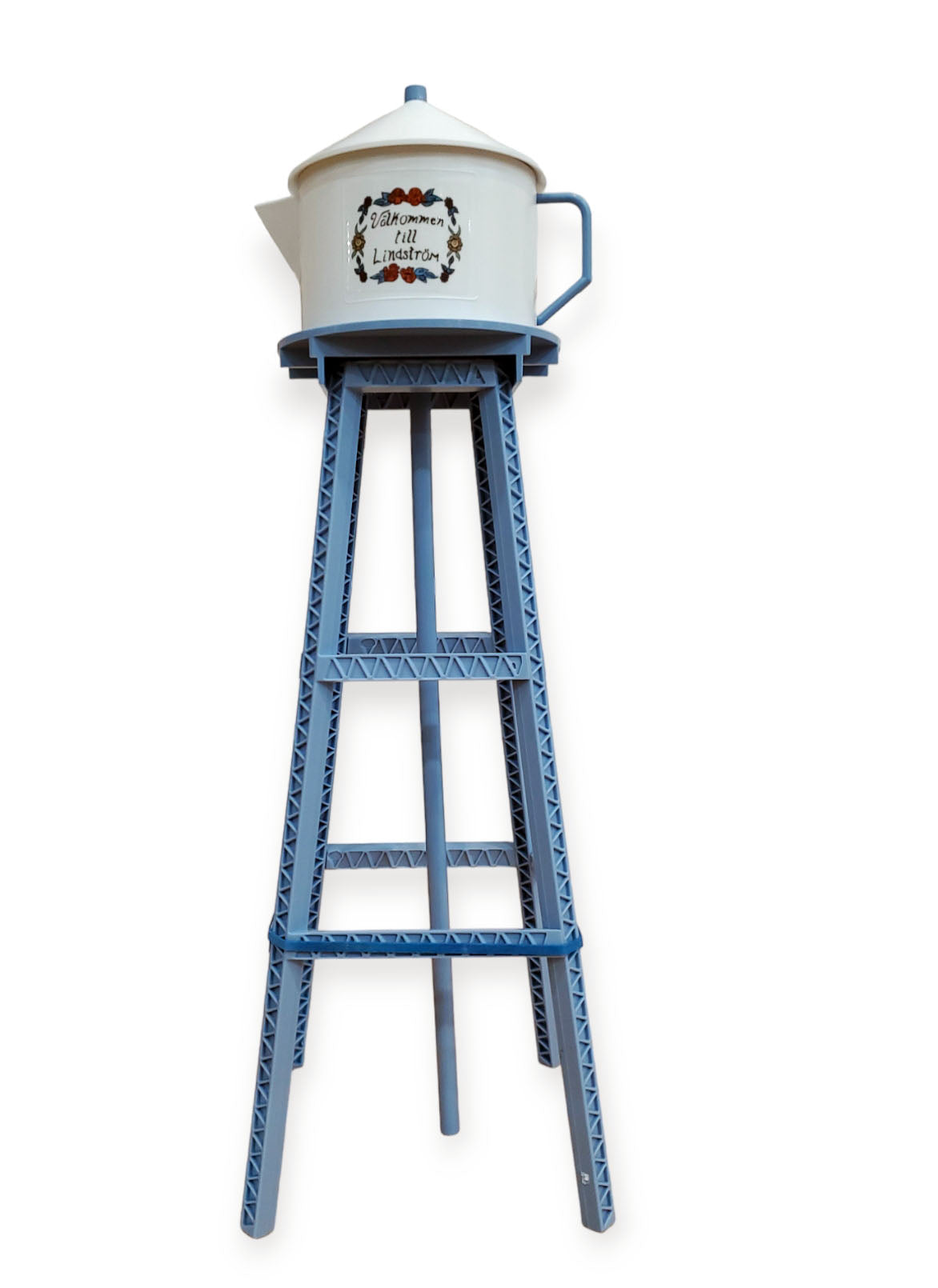 A Model Kit: Miniature Replica of the Lindström Coffee Pot Water Tower features a white teapot with floral decoration on a tall blue stand with geometric patterns, set against a white background.