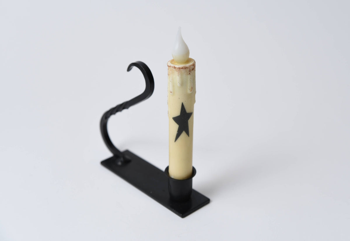Battery-operated taper candle with a black star design in a black iron holder with a curved handle.
