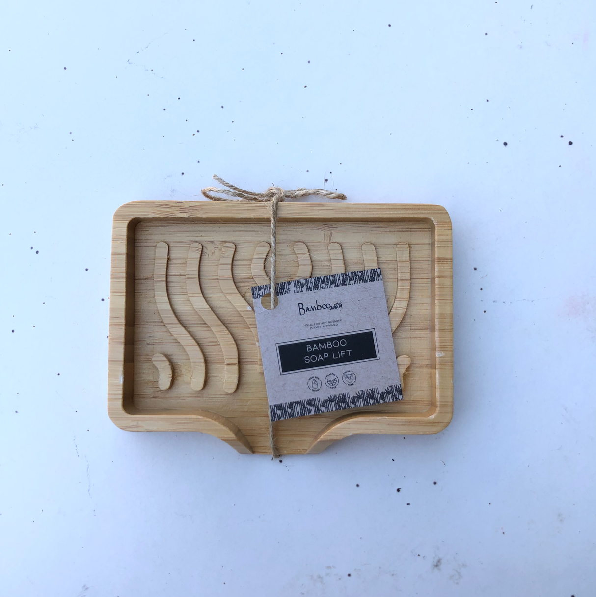 Rectangular bamboo soap holder with wave-shaped grooves, tied with twine, and labeled with a kraft paper tag.