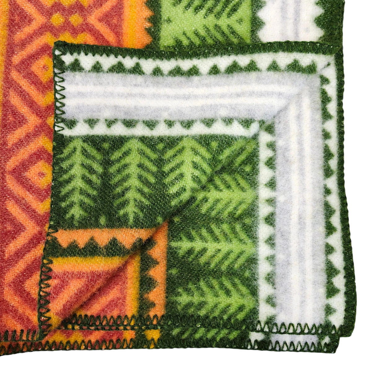Close-up of a folded blanket featuring green, orange, and white geometric and leaf patterns, visible stitched edge, and soft lambswool texture.