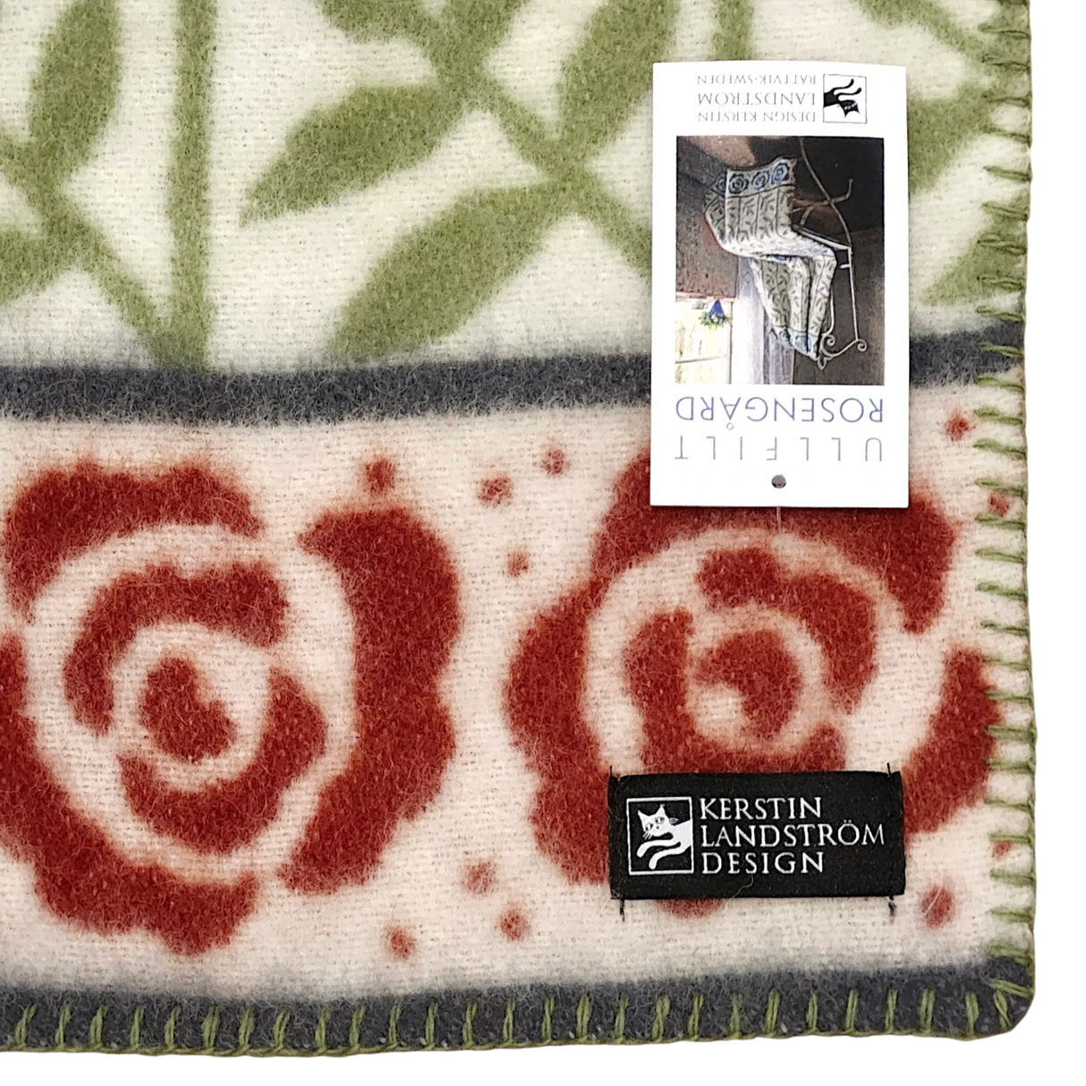 Lambswool blanket featuring red rose patterns with green leaves, plus two visible labels: one reads KERSTIN LANDSTRÖM DESIGN; the other shows product image and details.
