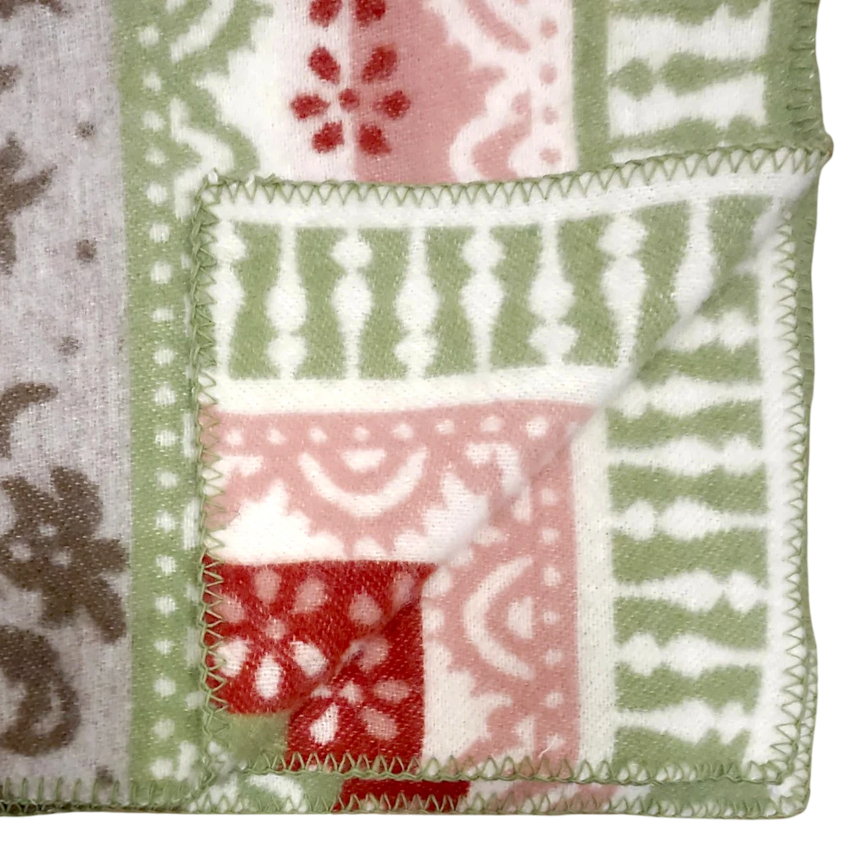 Folded corner of a fleece blanket featuring green, red, white, and beige geometric and floral patterns with zigzag stitching along the edge.