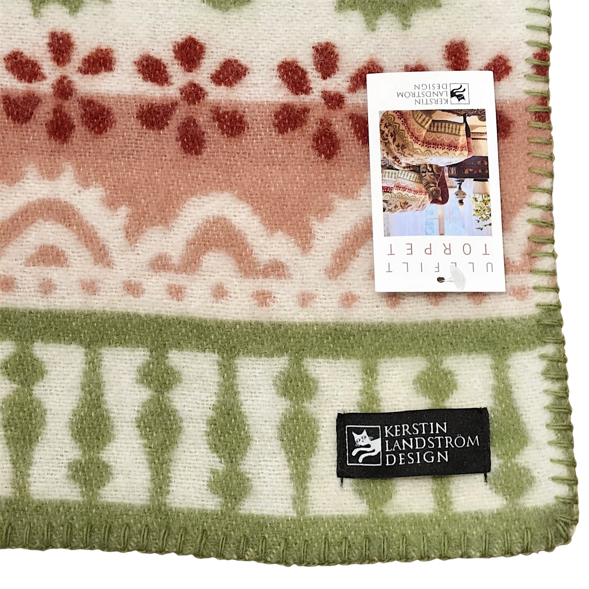 Swedish wool throw featuring green, red, and ivory patterns, with a product tag attached showing images of people wearing similar lambswool blankets.