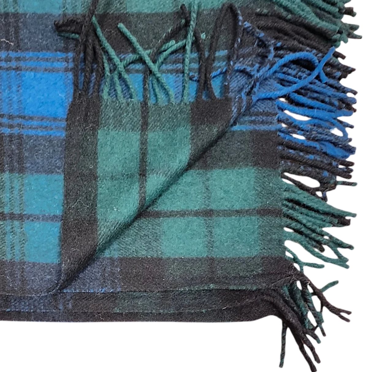 Folded blanket in Black Watch tartan with green, blue, and black stripes, showing fringed edges and one corner turned up.