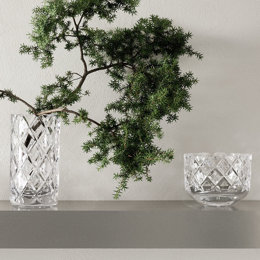 Crystal vases with geometric patterns showcase Gunnar Cyrens timeless artistry for Orrefors. One vase holds lush green foliage, while the other stands empty, reminiscent of the classic Orrefors Sofiero Bowl Medium.