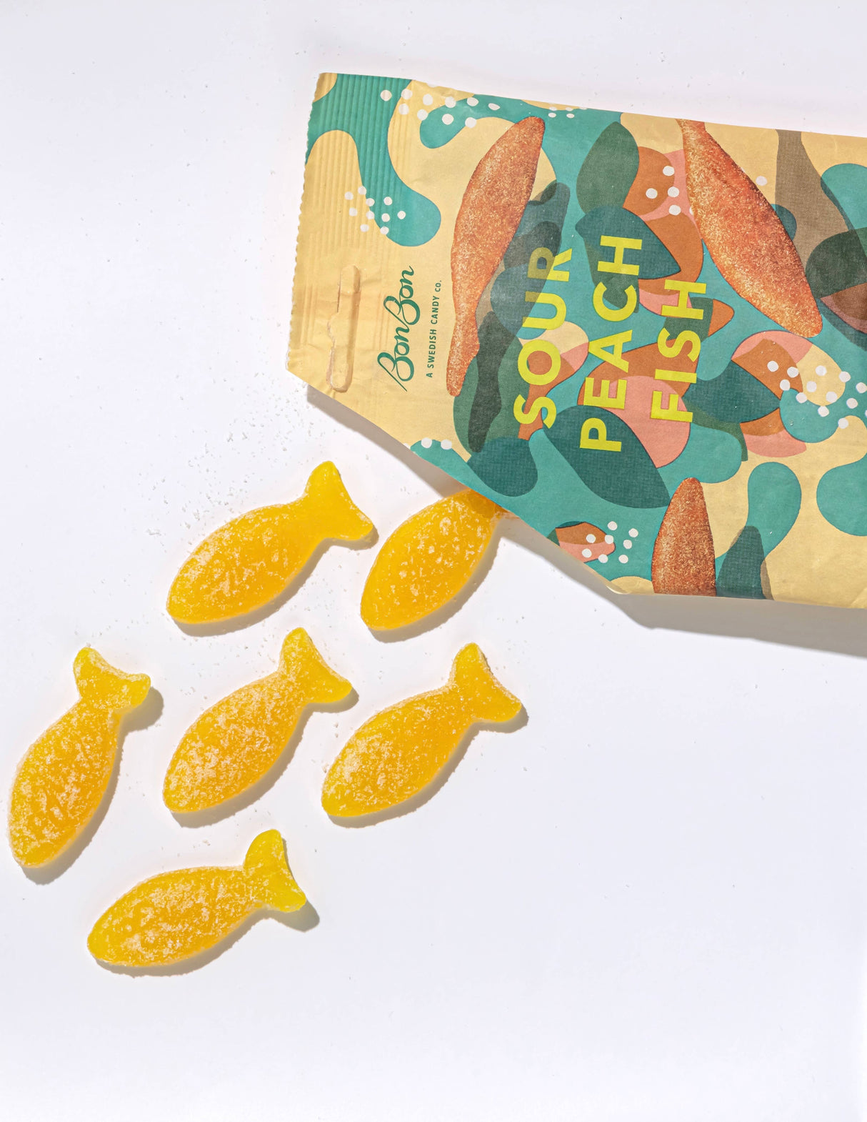An open package of BonBon Sour Peach Fish (150g) Swedish Candy displays six yellow, fish-shaped candies scattered on a white surface.