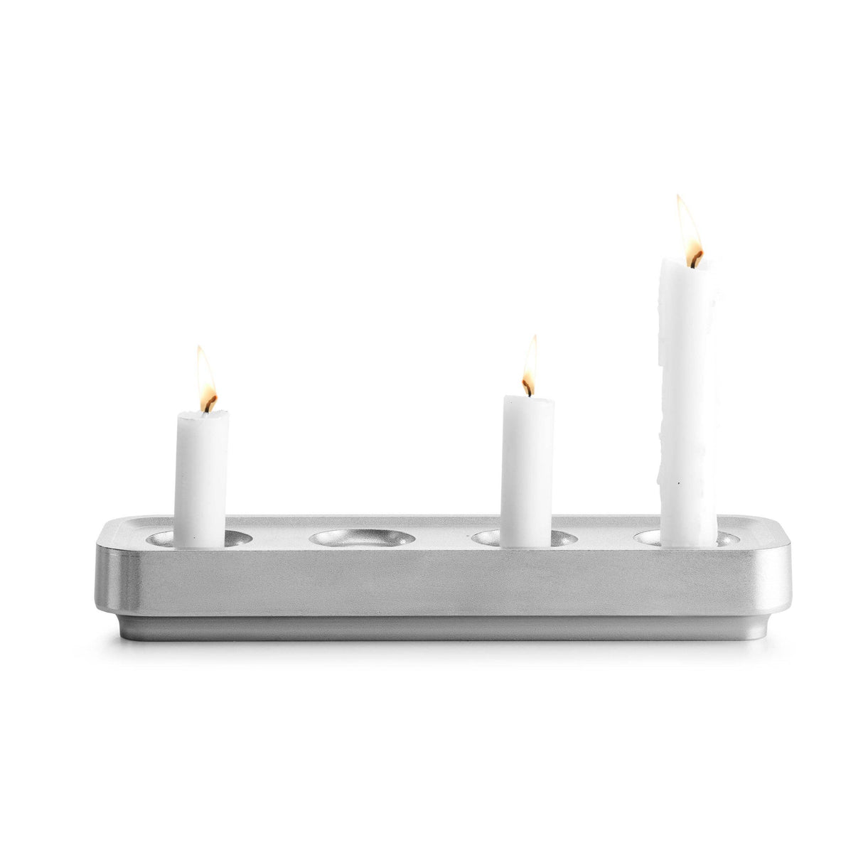 Three white candles, two short and one tall, are lit and elegantly placed in the sleek Stumpastaken Swedish Candle Holder, crafted from recycled aluminum with rounded edges.