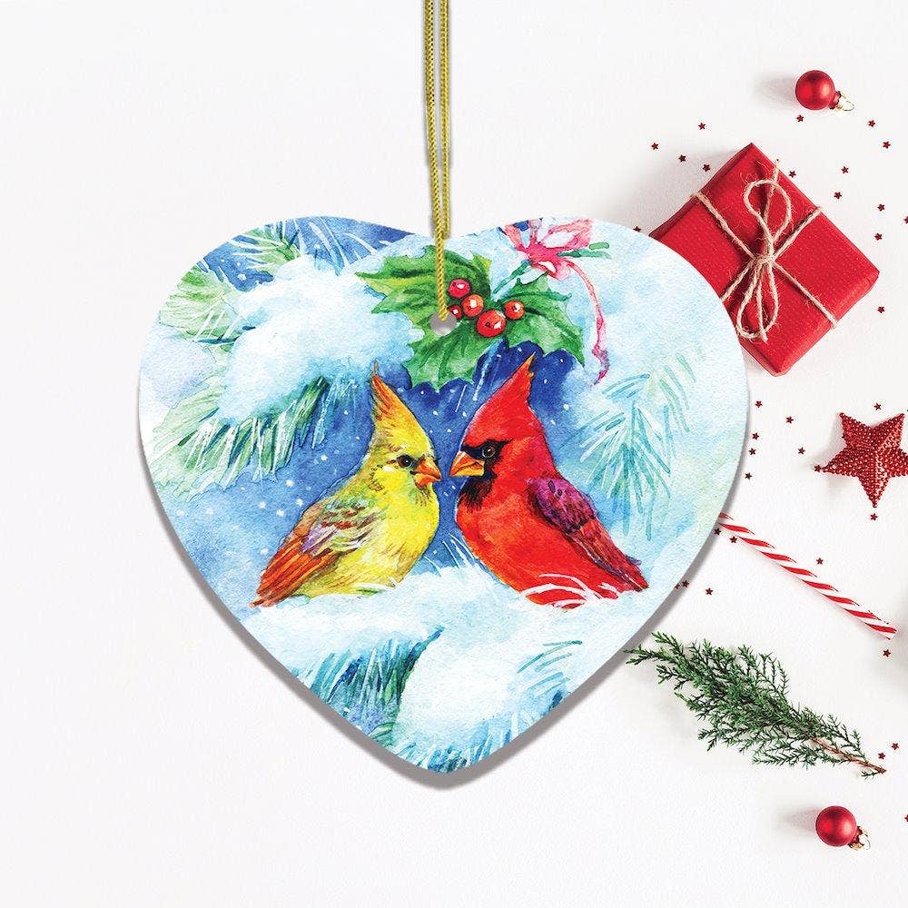 The Watercolor Cardinal Mistletoe Romance Christmas heart-shaped ornament features a cardinal on snowy branches, holly, a wrapped gift, star, and pine twig on a white background.
