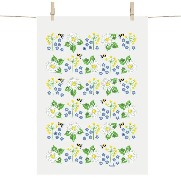 The Swedish Summer Flowers Tea Towel by Anneko Design Sweden hangs on a line, adorned with daisies, yellow and blue blooms, green leaves, and small bees in a vibrant floral pattern.