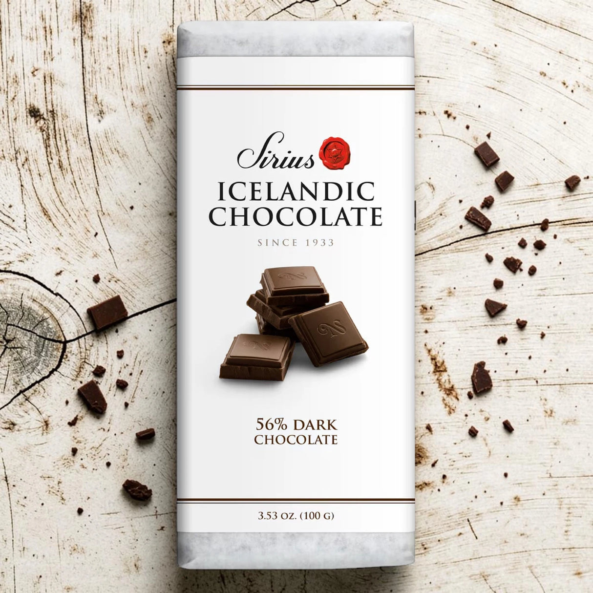 Nói Síríus chocolate bar wrapper with pieces of 56% dark chocolate on a wooden surface; visible text includes “3.53 oz (100g)”.