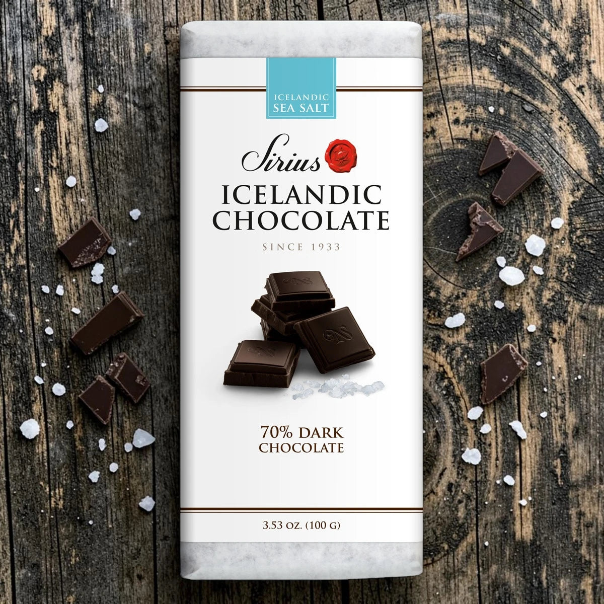 An Icelandic dark chocolate bar with sea salt on a wooden surface, broken pieces around it, and visible salt crystals scattered nearby.