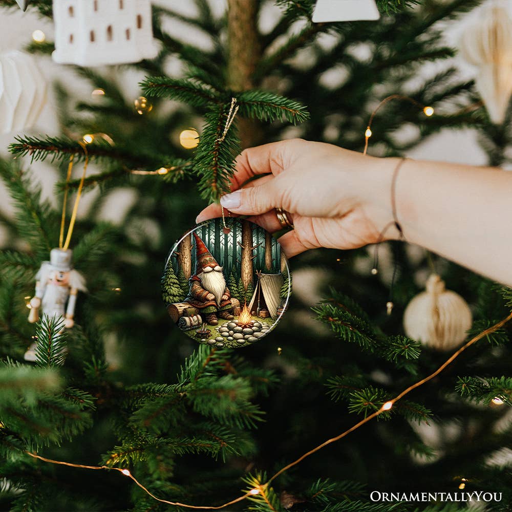 A hand places the Nordic Folk Gnome Forest Elder Themed Ceramic Ornament on a beautifully decorated Christmas tree with twinkling lights, infusing the festive scene with Scandinavian charm.