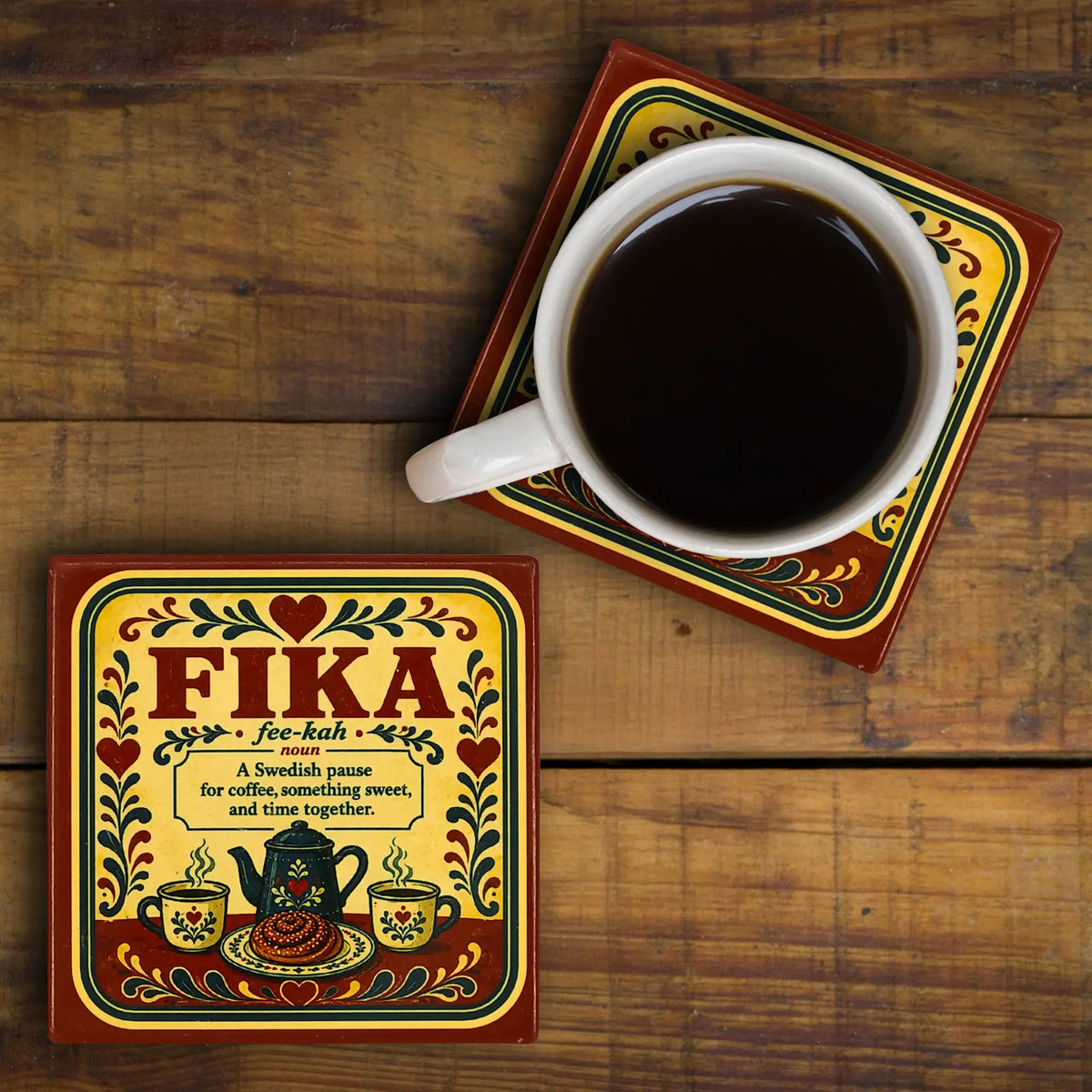 Two square coasters with Swedish rosemaling; one supports a coffee mug and the other displays a definition of Fika.