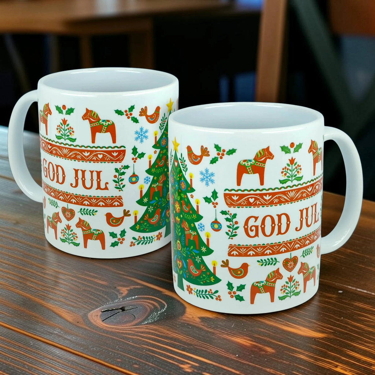 Two white "God Jul Dala Horse Christmas Ceramic Mugs" by Nordic Wholesale are displayed on a wooden table, each featuring festive Scandinavian motifs including horses, birds, hearts, trees, and the orange-printed phrase "God Jul," which means Merry Christmas in Swedish. These charming 11 oz ceramic mugs embody Nordic folk art and make a perfect addition to any Scandinavian holiday coffee cup collection.