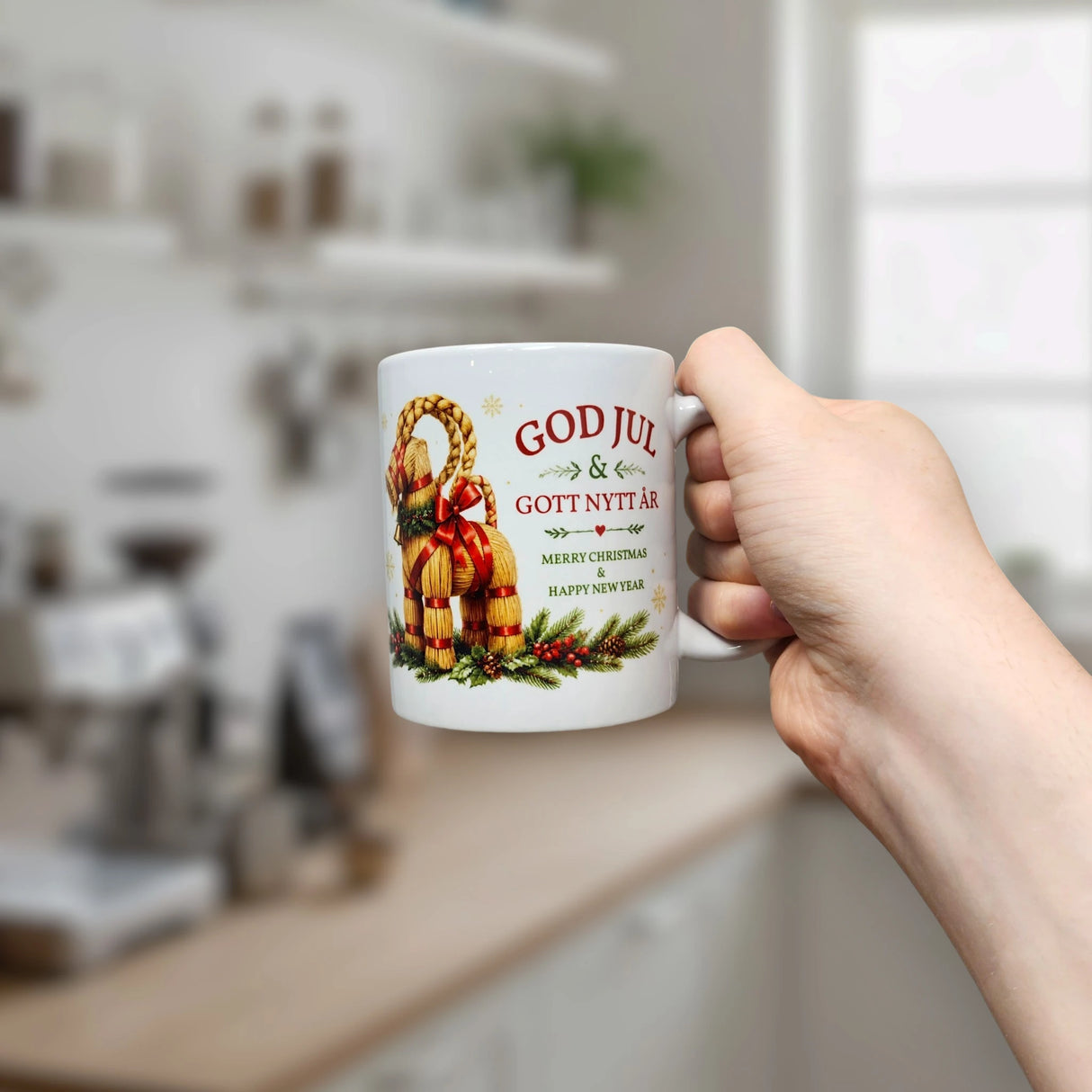 A hand holds the Nordic Wholesale Mug: God Jul Yule Goat Ceramic Mug (11 oz Capacity) in a kitchen. This festive mug features a classic Scandinavian Yule Goat surrounded by greenery, with “GOD JUL & GOTT NYTT ÅR” and “Merry Christmas & Happy New Year” printed on it—a charming choice for celebrating the holidays.