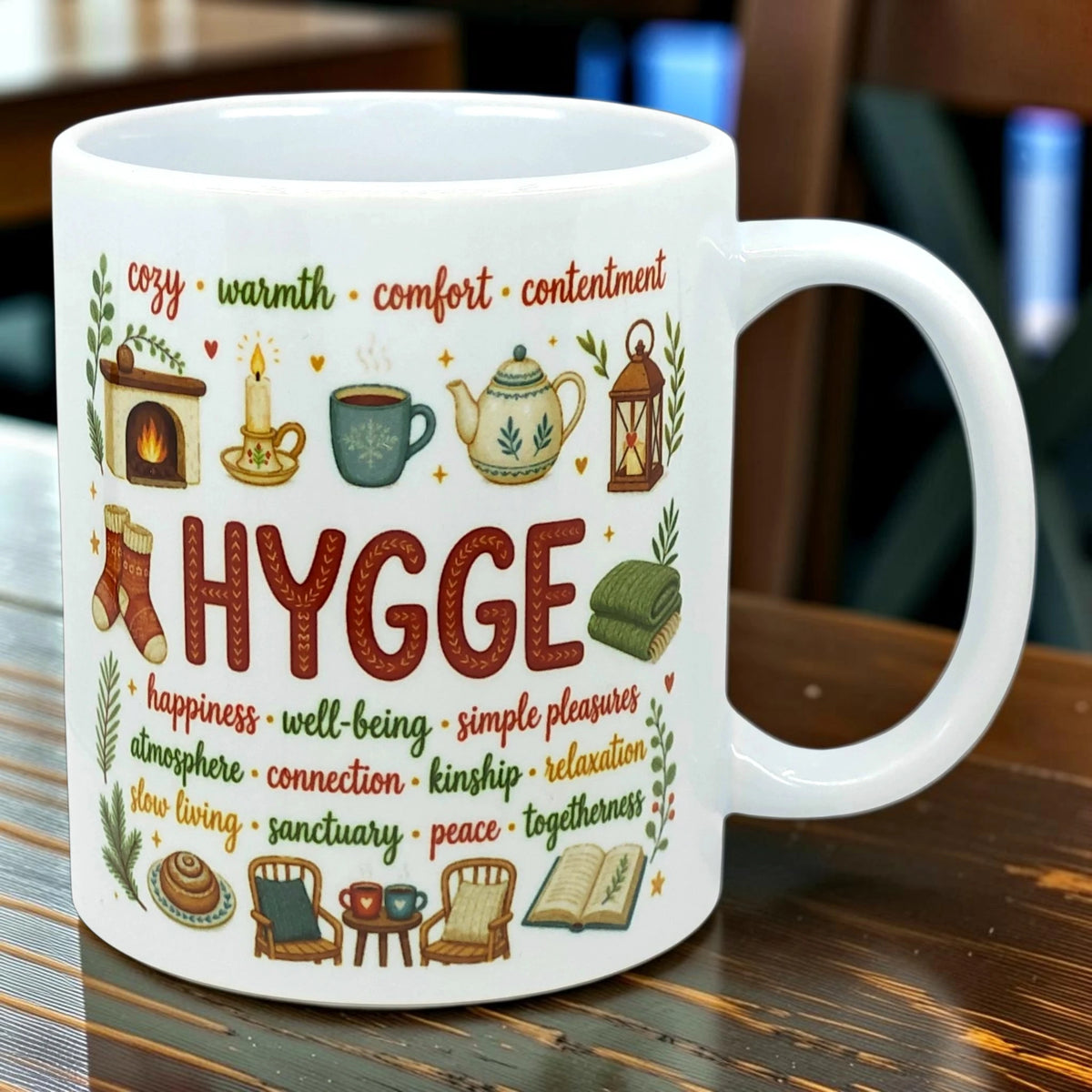 White Nordic mug with the word HYGGE, words such as cozy and warmth, and illustrations of a fireplace, tea cup, books, socks, and candles.