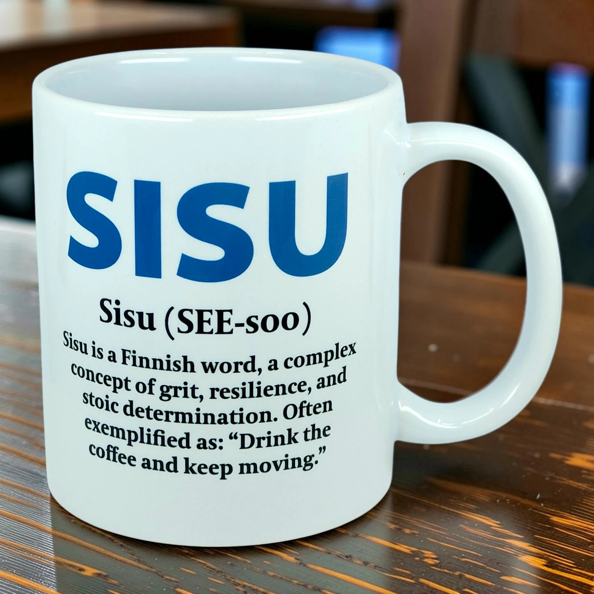 The Nordic Wholesale Mug: Sisu Finnish Word Definition Ceramic Mug (11 oz) is a white mug featuring the definition of "Sisu," a Finnish word meaning grit, resilience, and stoic determination, along with the example: "Drink the coffee and keep moving.
