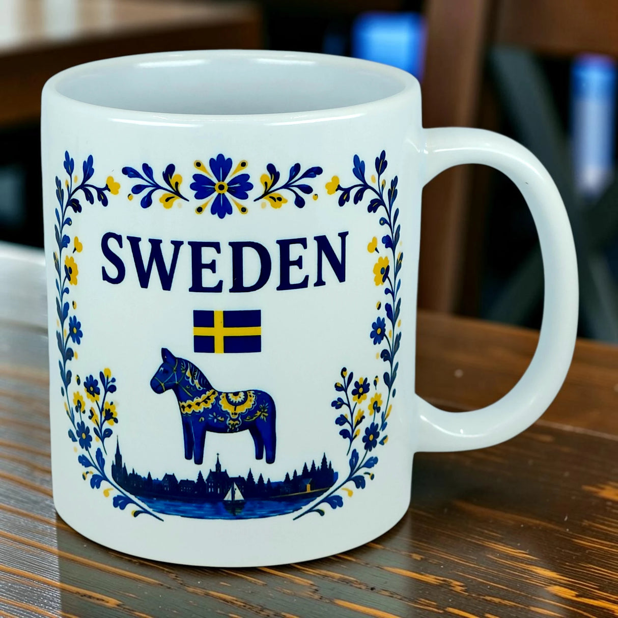 Introducing the Mug: Sweden Dala Horse Ceramic Mug (11 oz Capacity) by Nordic Wholesale—a white ceramic mug featuring "SWEDEN," a Swedish flag, and a classic blue Dala horse adorned with yellow and blue floral motifs. A cityscape silhouette lines the bottom edge, creating the perfect tribute to Scandinavian design and tradition for anyone celebrating Swedish heritage.
