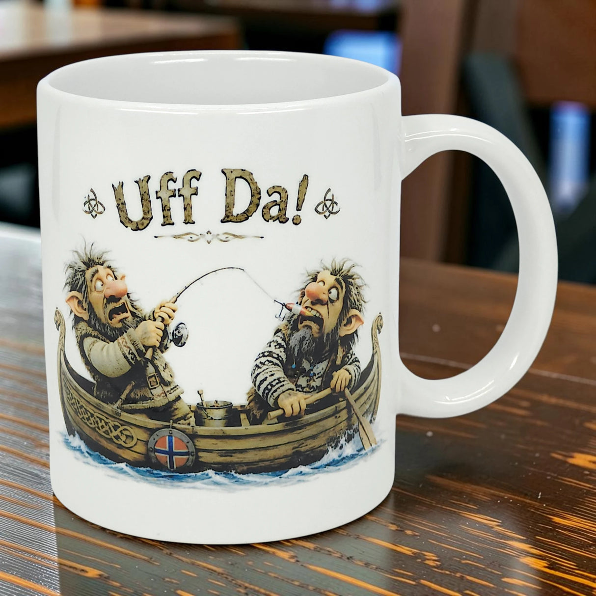 The Mug: Uff Da Fishing Trolls Ceramic Mug (11 oz) by Nordic Wholesale features two cartoon trolls fishing in a boat with a Norwegian flag and “Uff Da!” text—an ideal collectible for fans of Scandinavian designs.