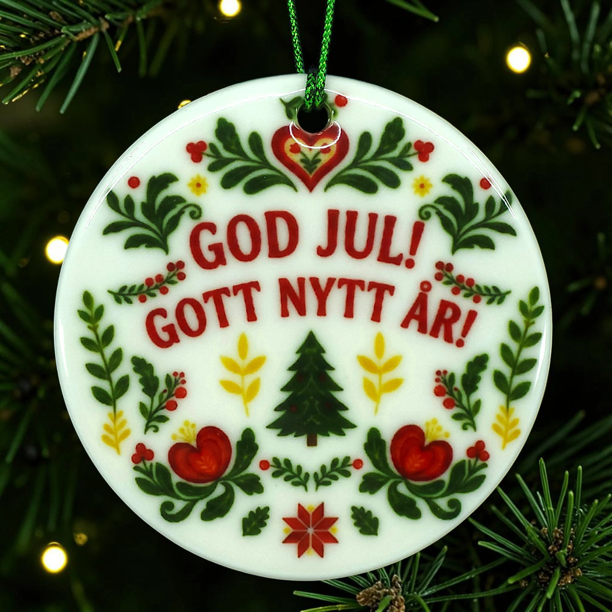 Round white ceramic ornament with a green and red folk-art Christmas tree pattern and the Swedish text GOD JUL! GOTT NYTT ÅR!.