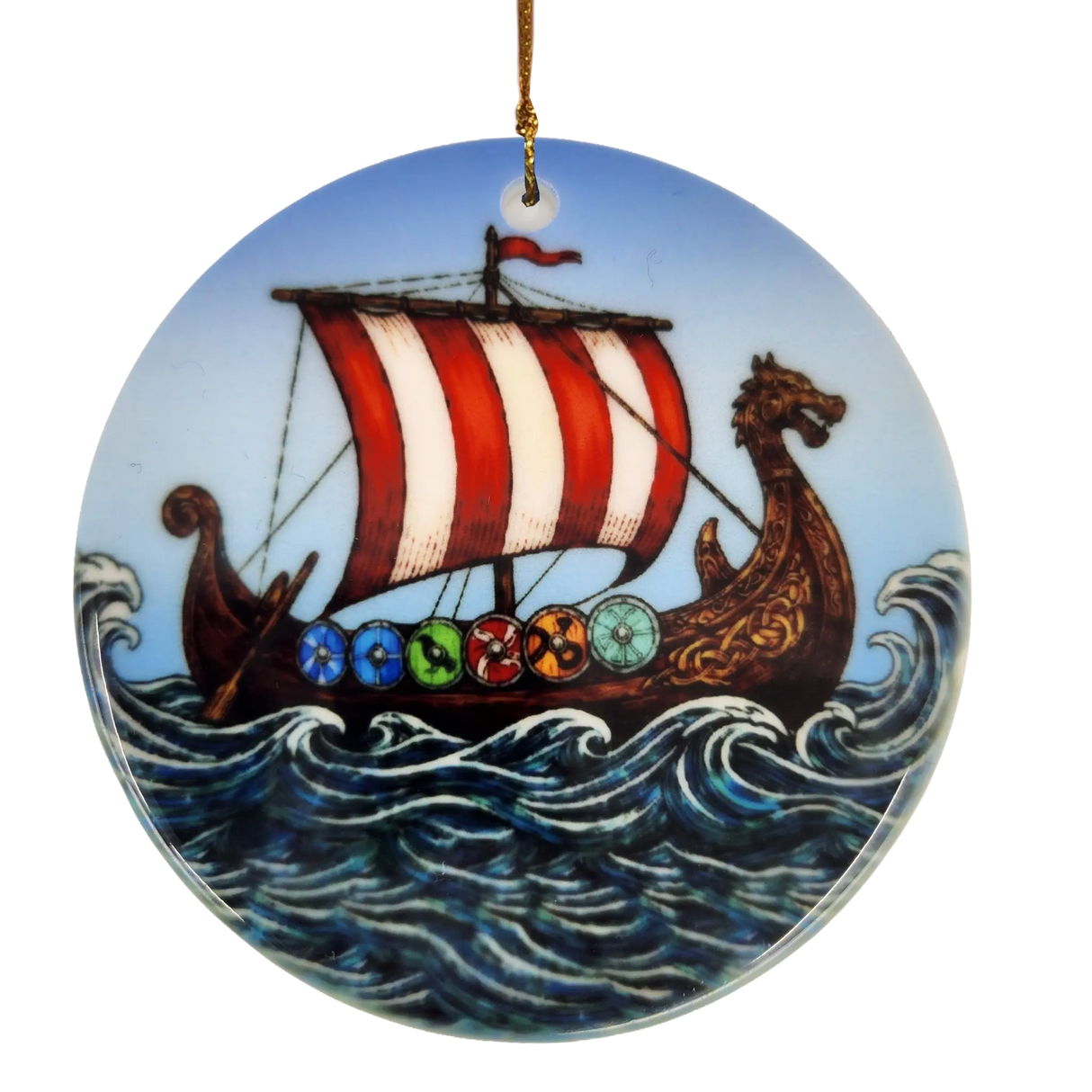 The Ornament: Viking Ship Ceramic Ornament (2.875" Diameter) by Nordic Wholesale features a round design depicting a ceramic longship with a red and white sail, dragon-shaped prow, and vibrant shields gliding through waves under a blue sky—perfect for creating striking Norse holiday décor. This ornament hangs elegantly by a gold string.