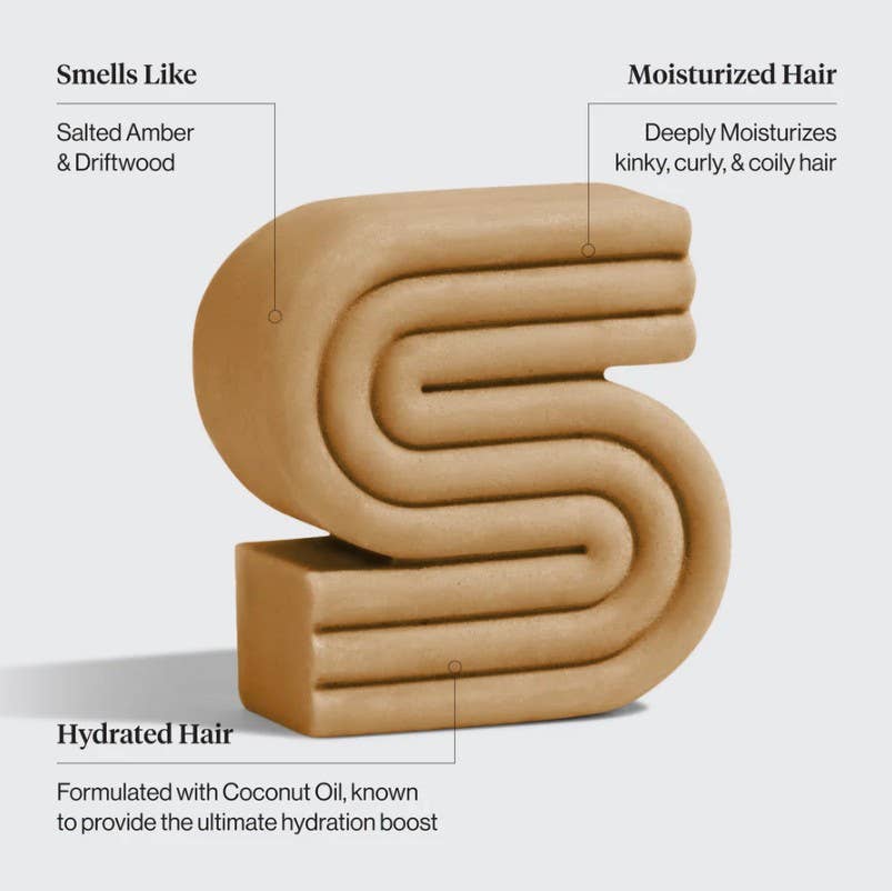 A tan, S-shaped bar labeled with its benefits—smells like salted amber & driftwood, moisturizes kinky and curly hair, and hydrates with coconut oil—KITSCH Coconut Oil Shampoo Bar for Dry Damaged Hair 3.2 oz is a luxurious moisturizing shampoo designed to nourish every coil.