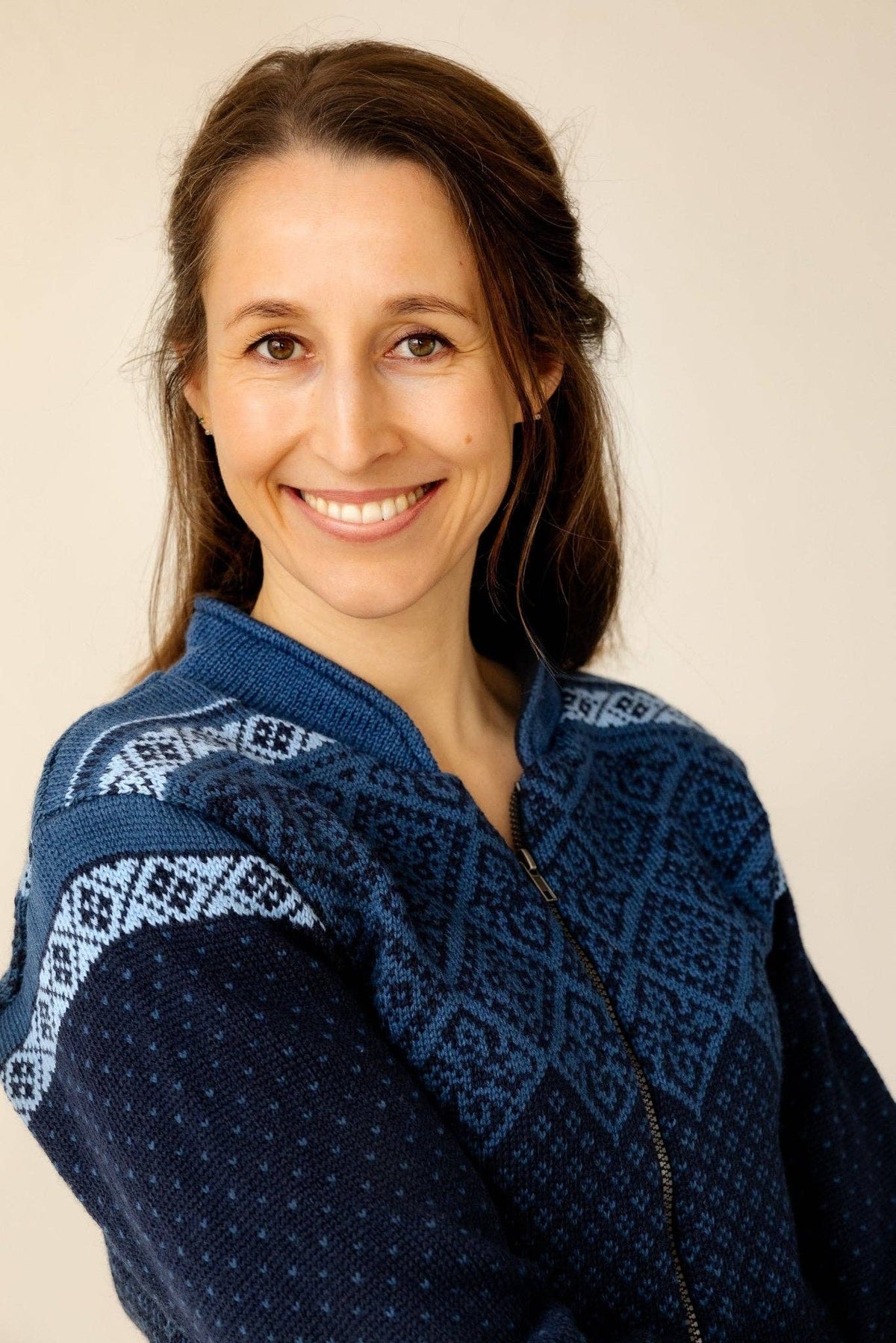 A woman wearing a zip-up sweater with a traditional Nordic geometric pattern across the shoulders and chest.