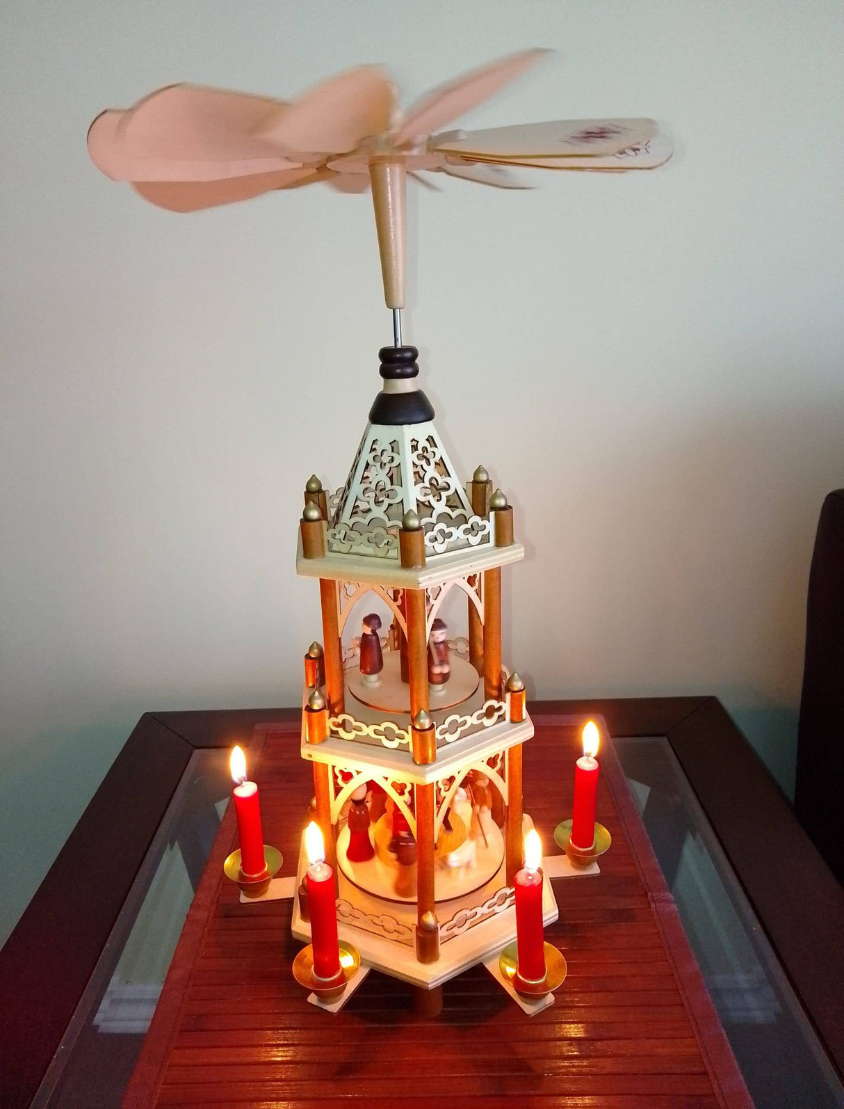 A wooden Christmas pyramid with spinning blades glows warmly on a table, lit by Red Christmas Pyramid Candles (Pyramiden-Kerzen, Box of 50, 14 x 70mm), adding traditional German holiday charm.