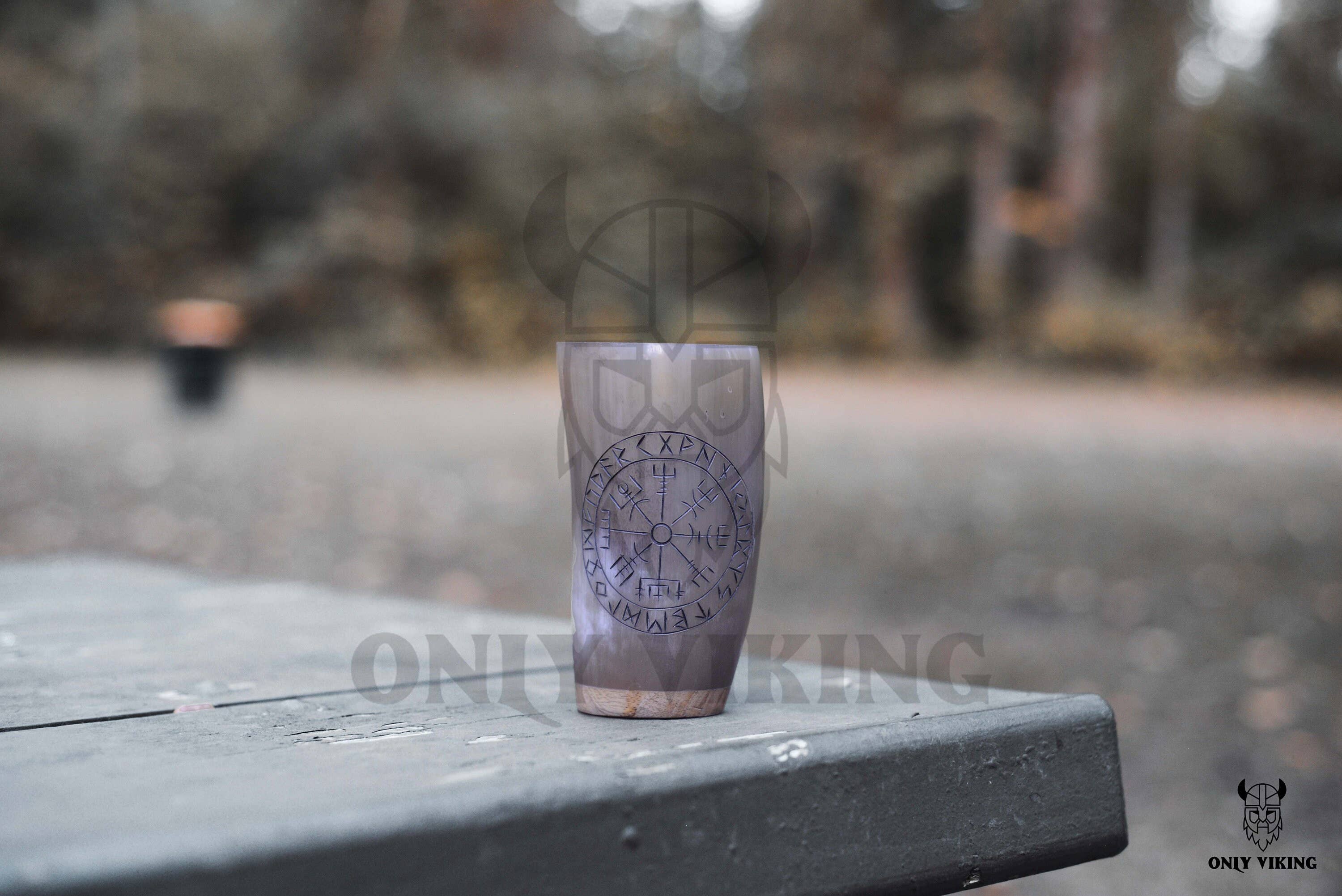 The Horn Mug: Beer Stein Drinking Horn Mug Tree of Life (6-9 oz) rests on an outdoor wooden table, its Viking-inspired design and intricate Tree of Life motif standing out against a blurred natural background.