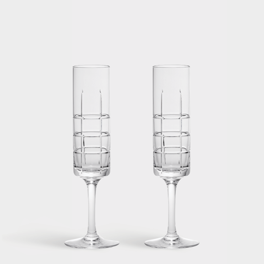 Two empty Orrefors Street champagne glasses, designed by Jan Johansson with grid patterns on their bowls, stand upright against a white background.