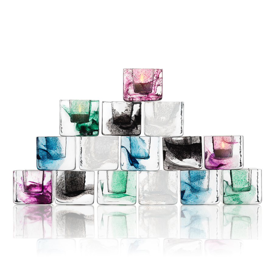 A pyramid of clear glass cubes, each with colored swirls, holds a lit KostaBoda: Brick Votive Candle Holder (available in 3 colors) by Anna Ehrner in the top cube.