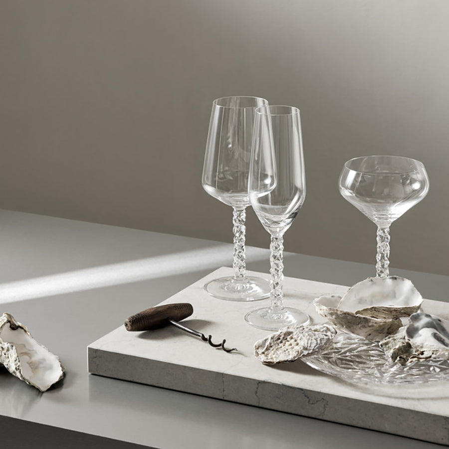 Two elegant Orrefors Carat Coupe 8.4oz crystal glasses sit on a table beside an oyster platter and corkscrew.