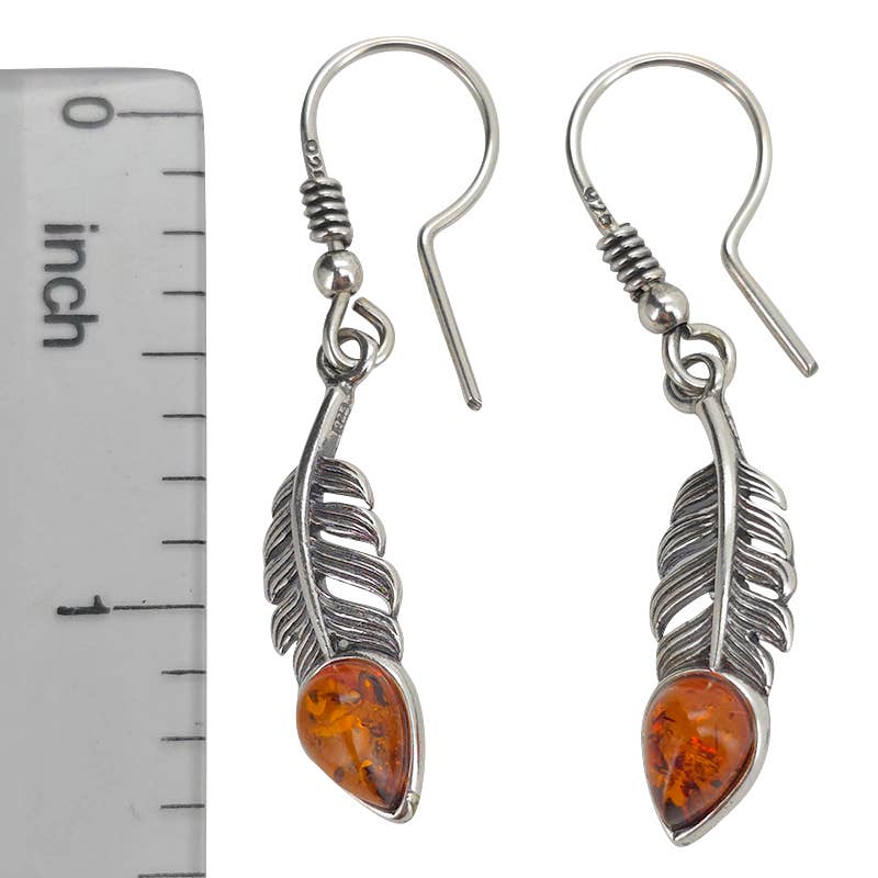 The Earrings: Amber Sterling Silver Feather Earrings On Hooks are shown beside a ruler for scale, measuring about 1.5 inches long, with teardrop Baltic amber accents highlighting the feather design.