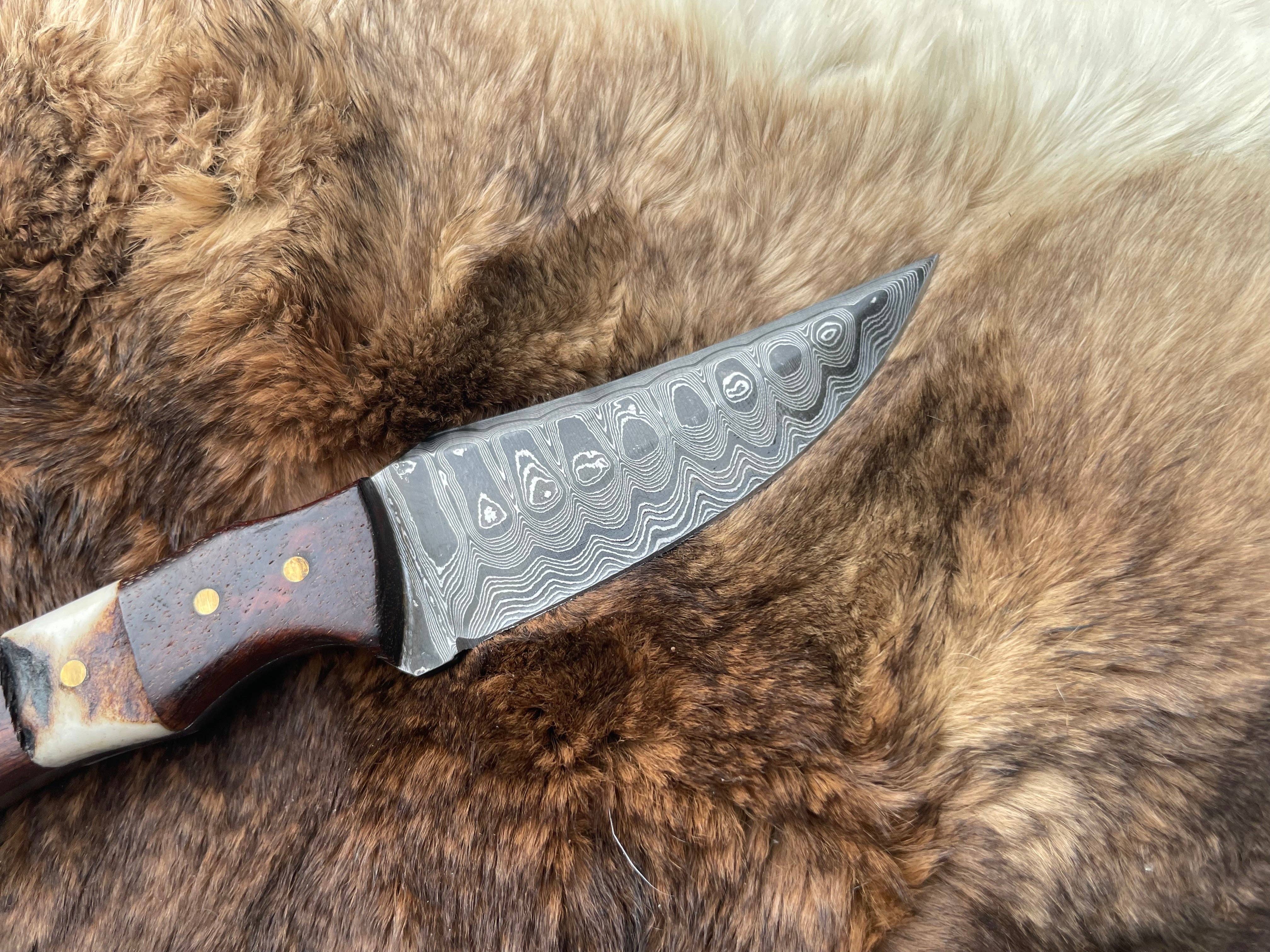 The Damascus Steel Skinner Knife with Rosewood & Stag Grip rests on a brown and white fur surface.