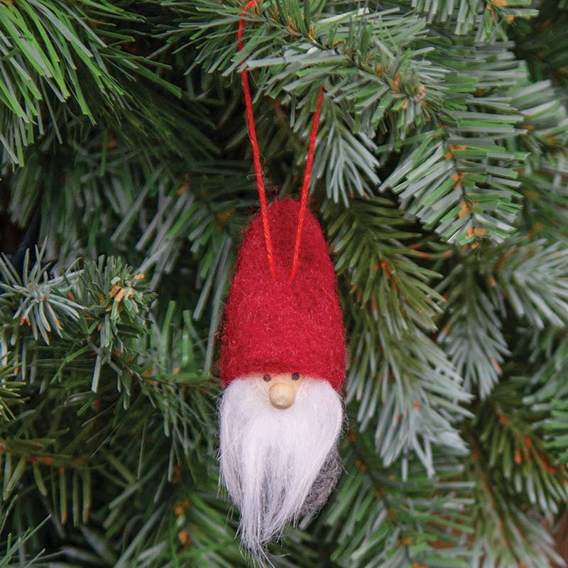The Ornament: Felted Mini Red Hat Tomte - Nisse - Gnome 3, featuring a white beard, hangs on a green pine tree branch as a charming Christmas decoration.
