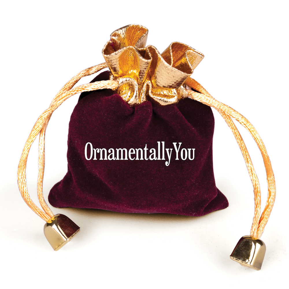 A burgundy velvet drawstring bag with gold trim featuring OrnamentallyYou, ideal for storing the Rustic Nativity Birth of Christ Scene Ornament, Christianity, made of sustainable ceramic.