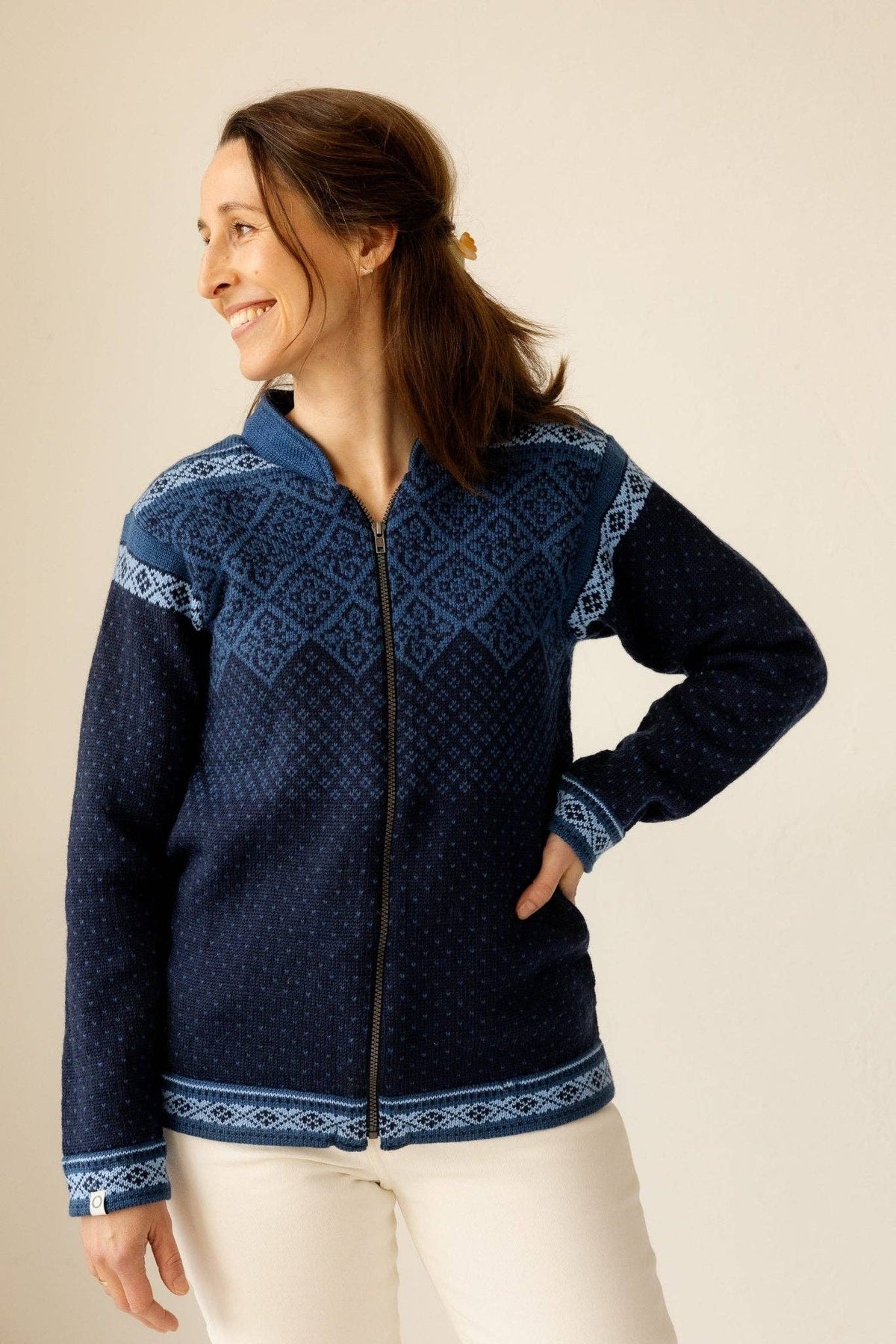 Woman wearing a wool zip-up sweater featuring a light blue Nordic geometric pattern on the chest and cuffs and a fleece-lined collar.