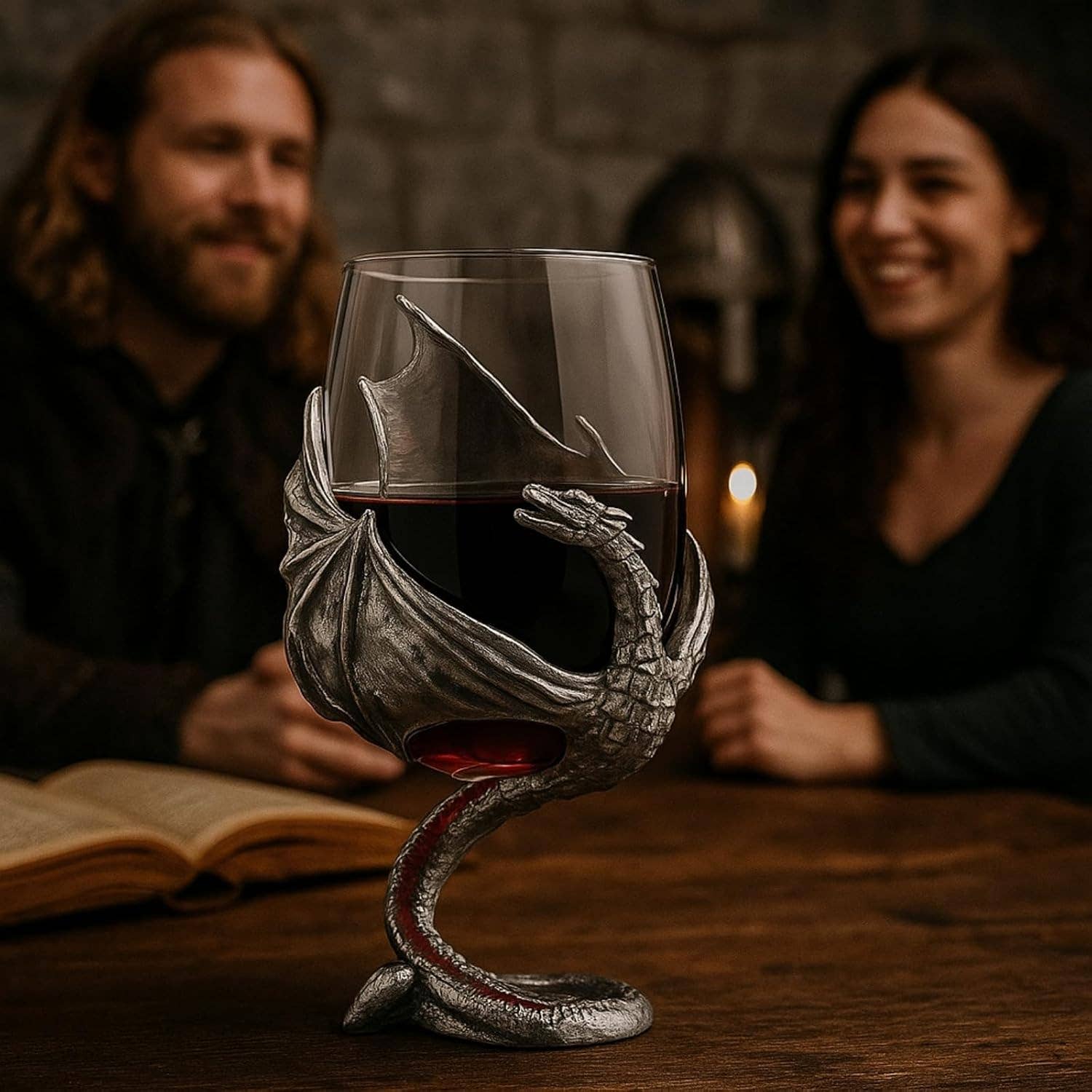 A Goblet: Medieval Dragon Viking Goblet Mug, 12oz sits on a table holding wine, with an open book and two smiling people in the blurred background—a great scene for fantasy drinkware fans.