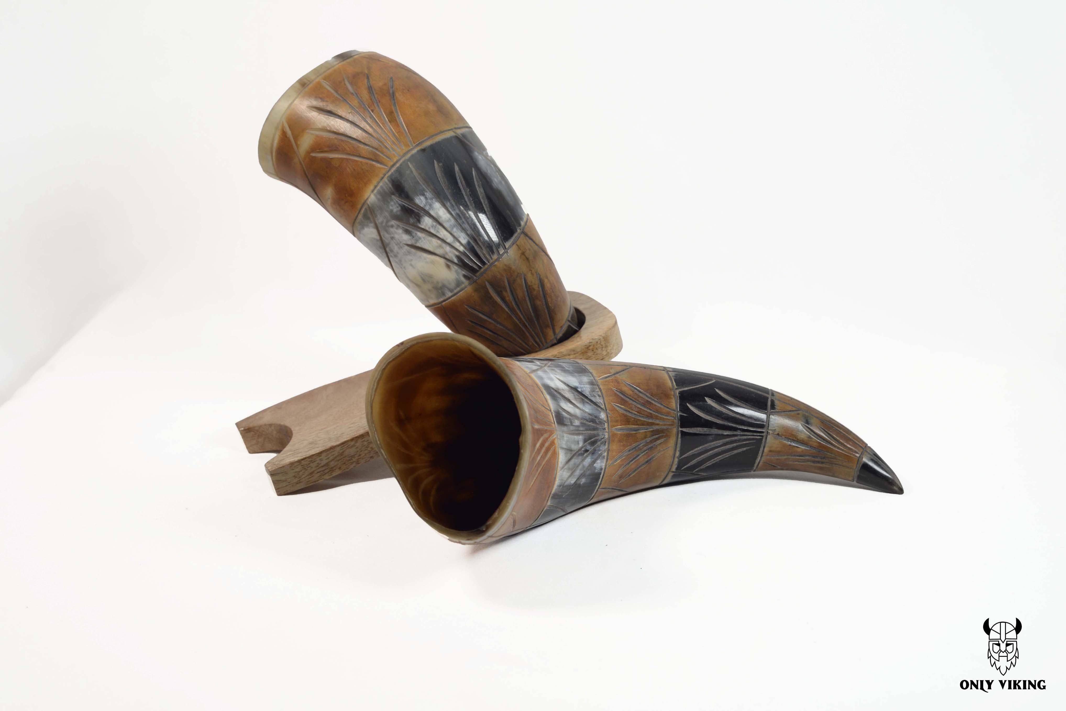 The Black & Brown Viking Drinking Horn set features two traditionally engraved ox horns on a wooden stand, showcasing black and brown patterns against a white background.