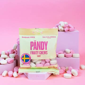 A package of Pandy Sugar Free Fruity Chews (1.8oz) is displayed in front of pastel pink blocks, with pink and white candies scattered on a pink background.