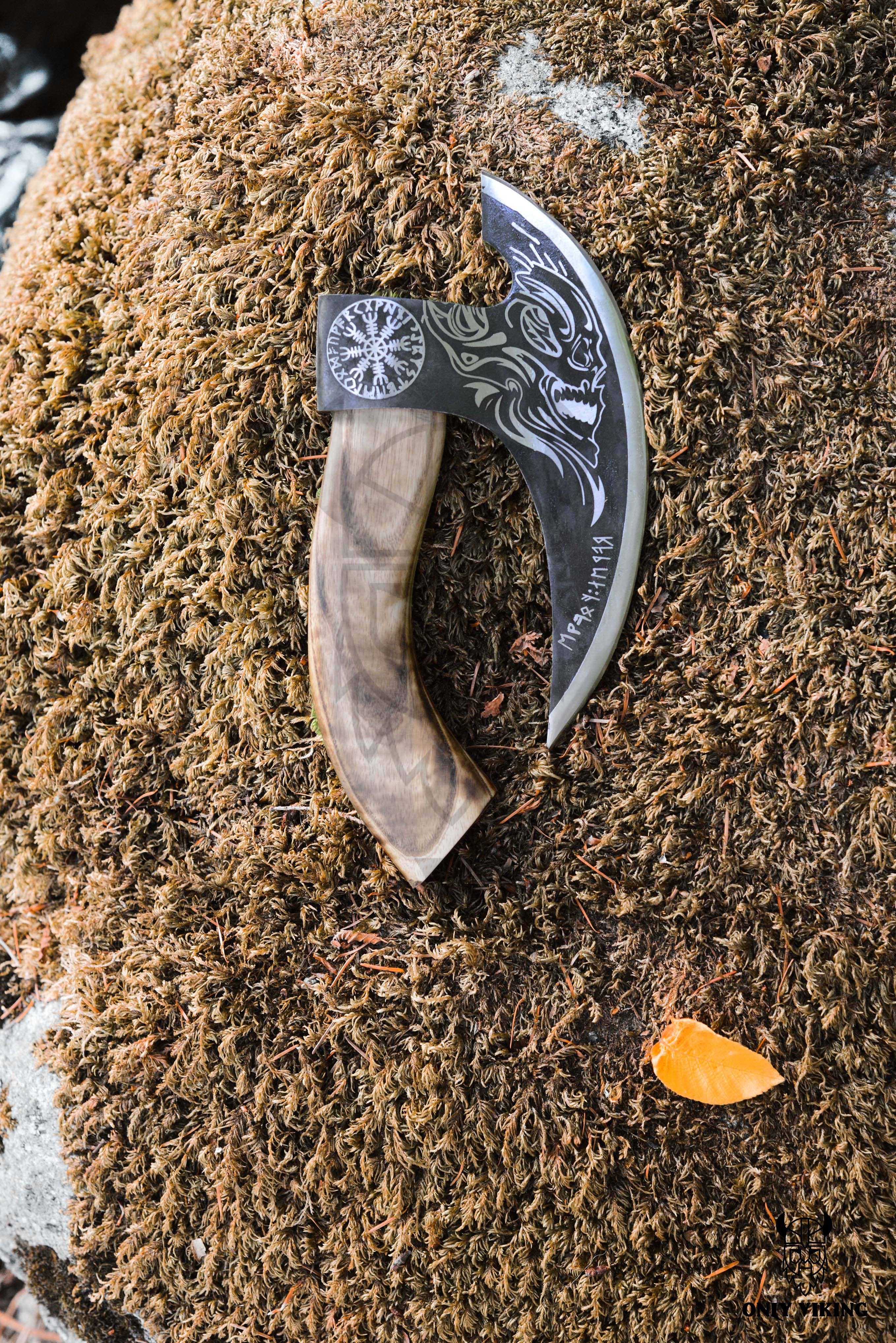 A decorative Pizza Cutter: Axe & Leather Axe Sheath with a curved stainless steel blade and wooden handle rests on a mossy rock, next to an orange leaf.